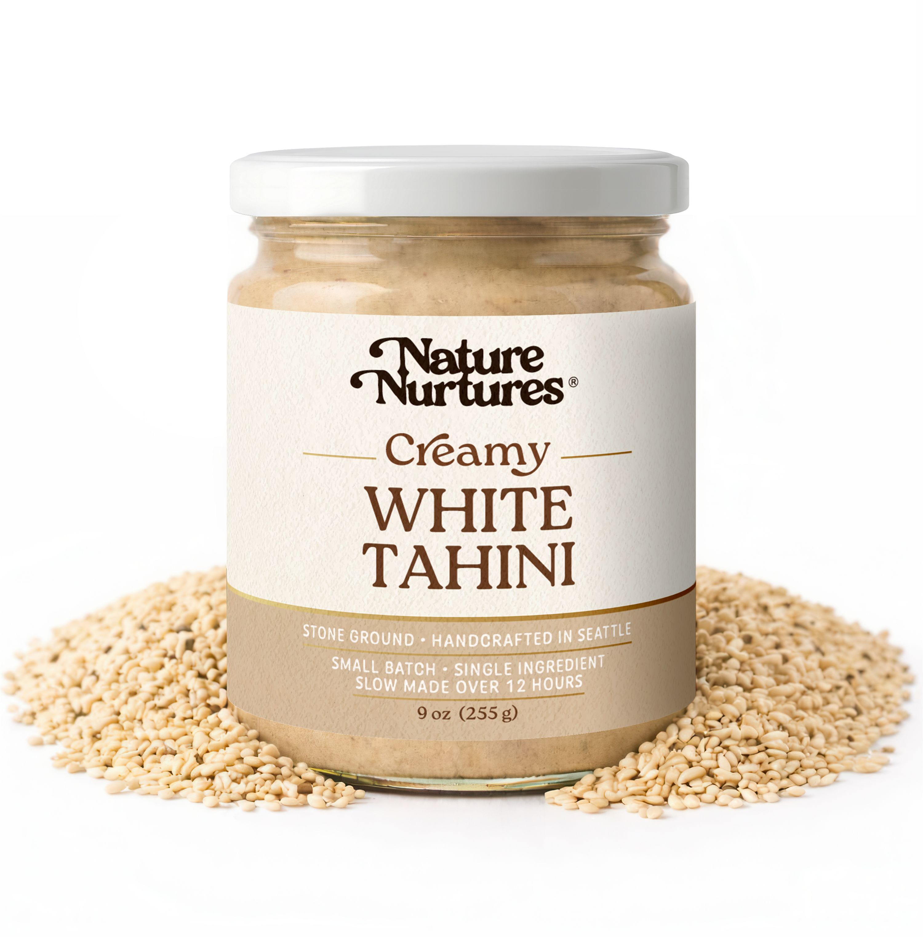May include: A jar of creamy white tahini, surrounded by sesame seeds. The label reads "Nature Nurtures Creamy White Tahini." The jar contains 9 oz (255 g) of tahini, stone ground, handcrafted in Seattle, and made slowly over 12 hours.